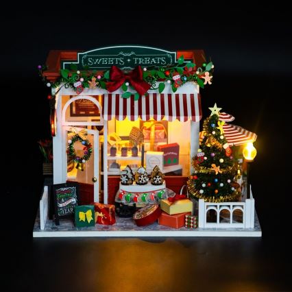 Miniatúrny vianočný obchodík s cukrovinkami a pochúťkami predáva sladkosti. V okolí je vianočný stromček, darčeky a nápis „Christmas & Happy New Year“.