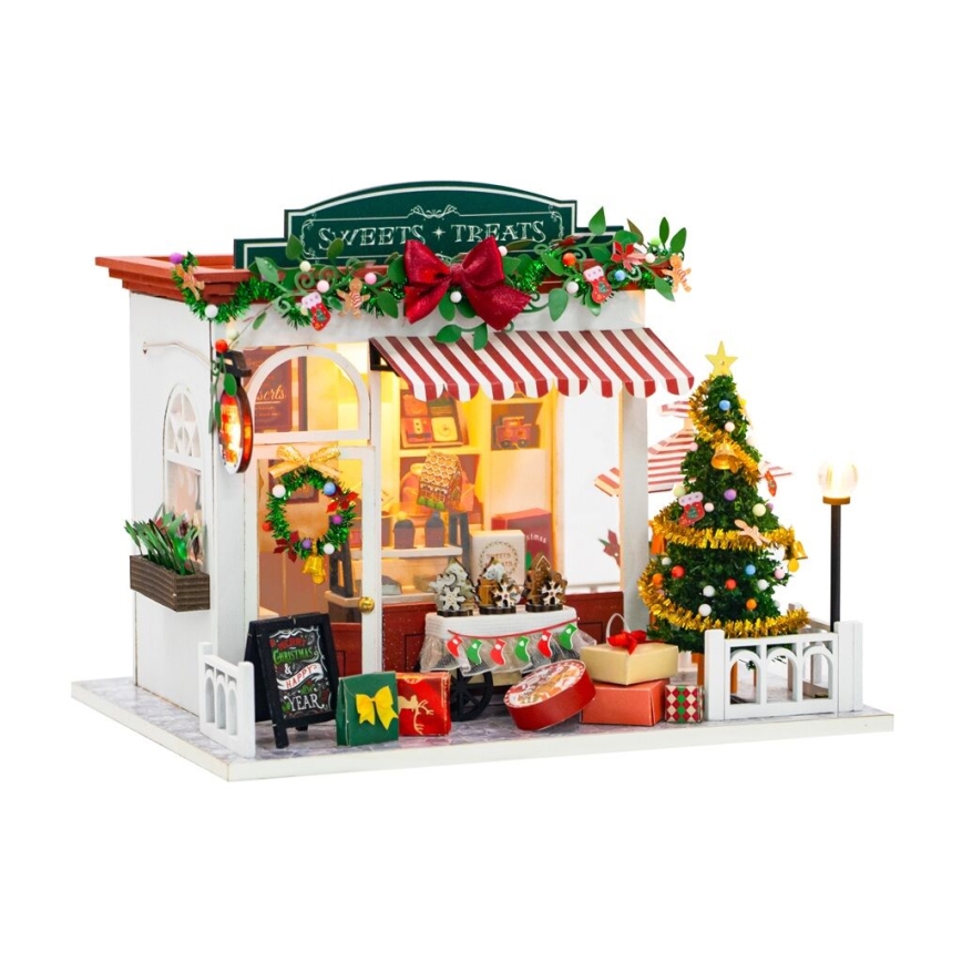 Miniatúrny vianočný obchodík – „Sweets + Treats“ – predáva sladkosti a pochúťky. Vianočný stromček a darčeky sú pred obchodíkom. Na tabuli je nápis: „Christmas & a Happy New Year“.