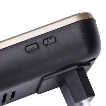 Zvoniaca jednotka s dvoma tlačidlami – jedno pre nastavenie hlasitosti a druhé pre výber melódie – je pripojená k elektrickej sieti. Má horný zlatý panel a čierny spodok.