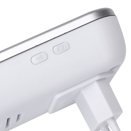 Biely bezdrôtový zvonček s dvomi tlačidlami: jedno pre zapnutie/vypnutie zvuku, druhé pre výber melódie. Je pripojený k elektrickej zásuvke.