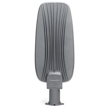 Sivá pouličná lampa s vertikálnymi drážkami na zadnej strane je umiestnená na krátkom stĺpiku. Lampa stojí na bielom pozadí.