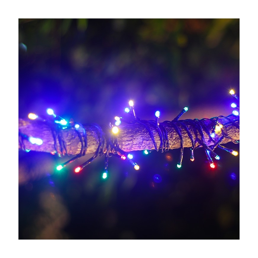 Elektrické svetielka rôznych farieb sú omotané okolo konára stromu v tme. Svietia modrou, červenou, zelenou a žltou farbou. Konár je hnedý a nachádza sa v exteriéri.