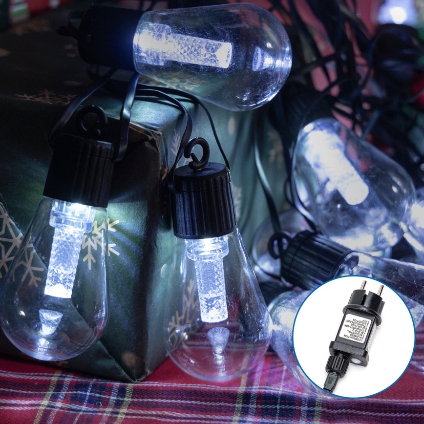 LED svetelný reťaz s objímkami v tvare žiaroviek svieti. Reťaz je umiestnená na darčekovej krabičke s vianočným vzorom na kockovanom stole. Na obrázku je tiež viditeľný adaptér s technickými údajmi: INPUT: 220-240V~50/60HZ 0.15A, OUTPUT: 31V 0.2A.