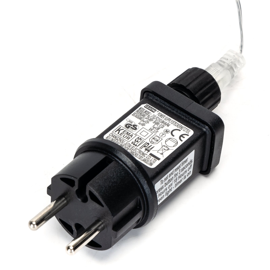 Sieťový adaptér s vidlicou a káblom je pripojený k svetelnému zdroju. Na adaptéri je text: POWER SUPPLY/STECKERNETZTEIL, MODEL MODELL, GS, KEMA SEL/IP44, EUR, CE, CHANGZHOU JUTAI ELECTRONIC CO.,LTD, To set and reset timer press button for 3 seconds Hours on 18 Hours off Even Light - timer is ove. Adaptér leží na bielom podklade.