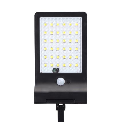 Solárny LED svietiaci panel s 36 LED diódami a pohybovým senzorom je pripevnený na čiernom stojane. Svietidlo svieti svetlom. Je umiestnené na bielom pozadí.