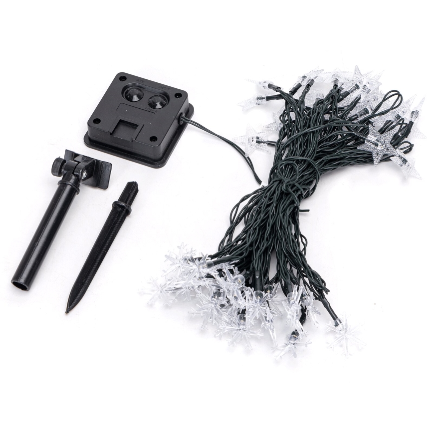 Solárny svietiaci bod s panelom na vrchu, na čiernej tyčke zapichnutej do zeme. Na kábli je štítok: GOOSTAR 20 LED SOLAR LIGHT, MODEL 2020AA, 200MA, FC/ASTER 120M, CA/LOT 240806-12, DC12V 0.08W, ONLY WET LOCATION.