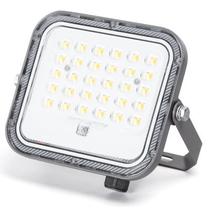 LED reflektor svieti. Má štvorcový tvar, sivú konštrukciu a obsahuje množstvo malých LED diód. Je umiestnený na nastaviteľnom stojane.