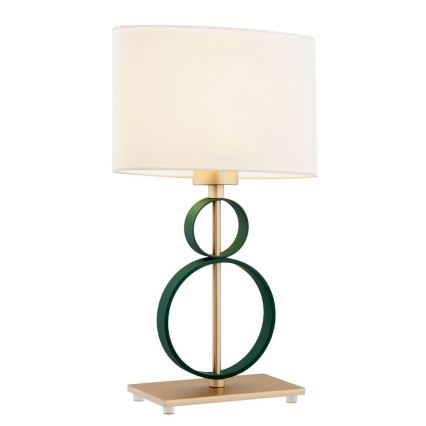 Stolová lampa s bielym tienidlom osvetľuje priestor. Základňa lampy je zlatá s tmavozelenými kovovými prvkami v tvare prepletených kruhov.