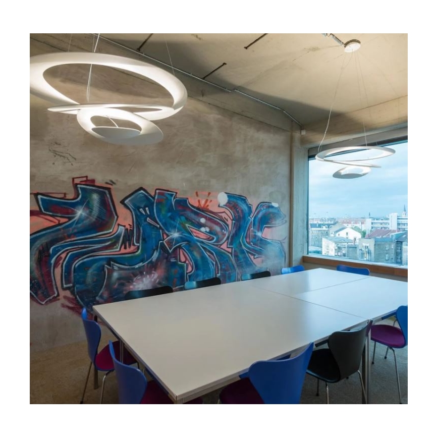 Dve moderné kruhové svietidlá osvetľujú konferenčný stôl v miestnosti s graffiti na stene a výhľadom na mesto cez veľké okno.
