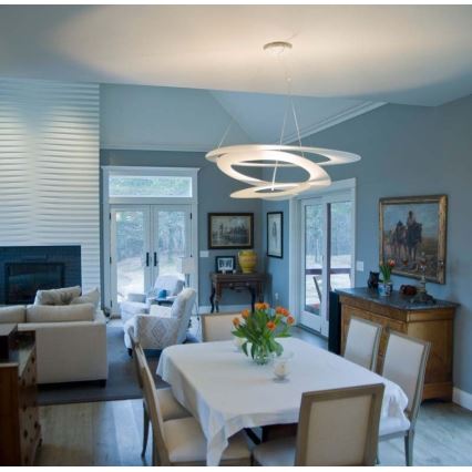 Moderná biela lampa visí v jedálni. Lampa osvetľuje stôl so stoličkami a kvetmi. Interiér je svetlý, s drevnou podlahou a bledomodrými stenami.