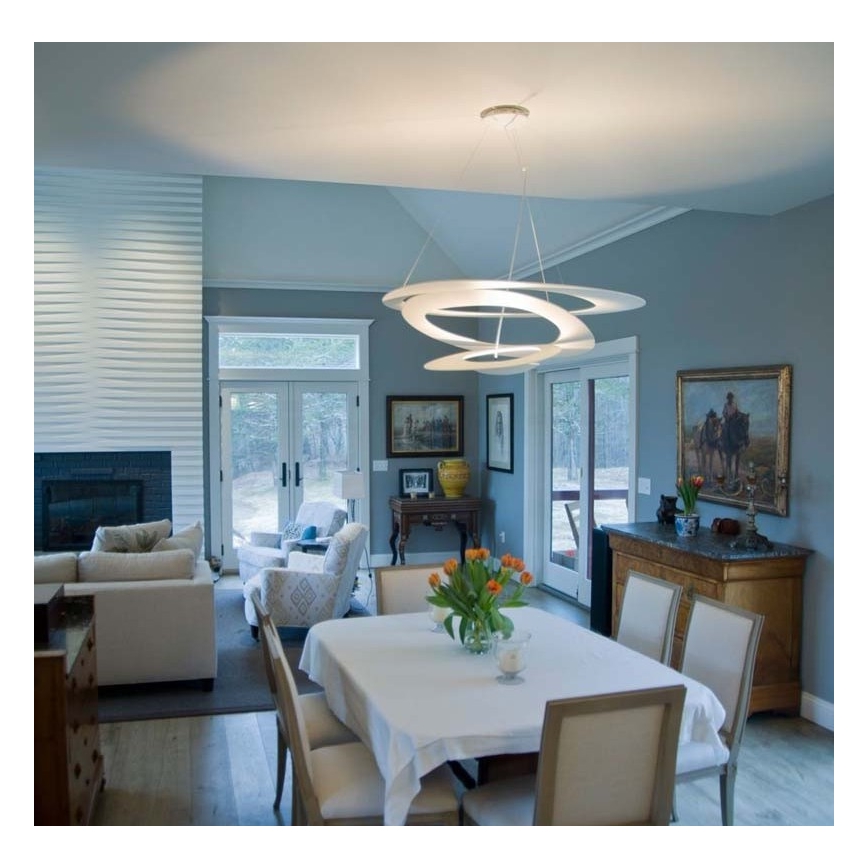 Moderná biela lampa visí v jedálni. Lampa osvetľuje stôl so stoličkami a kvetmi. Interiér je svetlý, s drevnou podlahou a bledomodrými stenami.