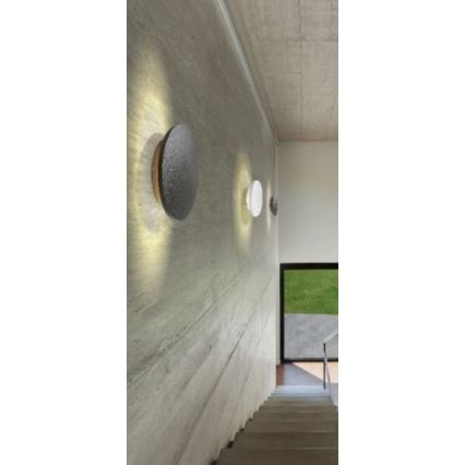 Tri nástenné svietidlá svietia na betónovej stene schodiska. Svietidlá sú okrúhle, rôznych farieb. Za schodiskom je vidieť okno s výhľadom na trávnik.