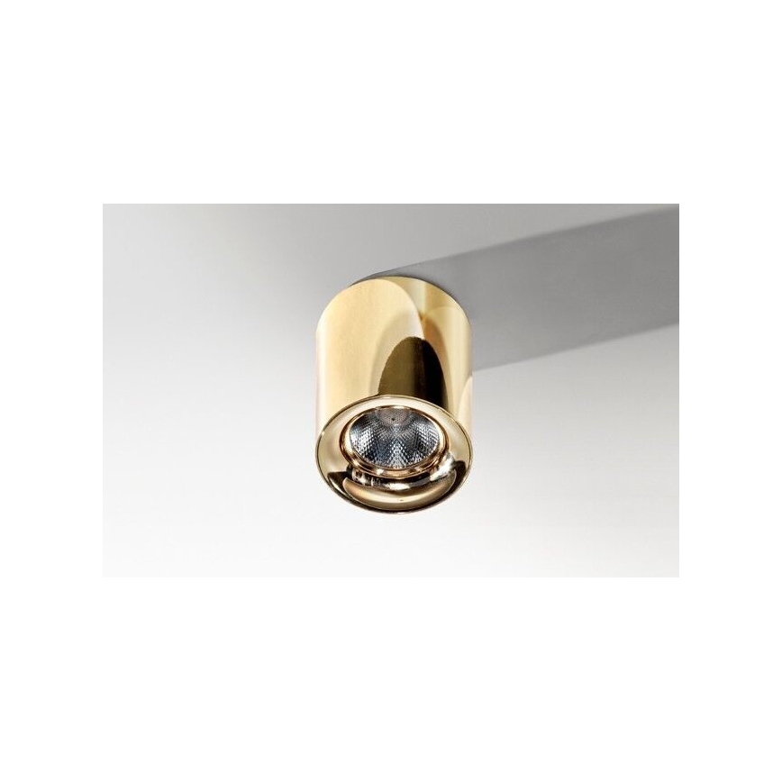 Zlaté svietidlo svieti. Je pripevnené k stropu. Svietidlo má valcovitý tvar.