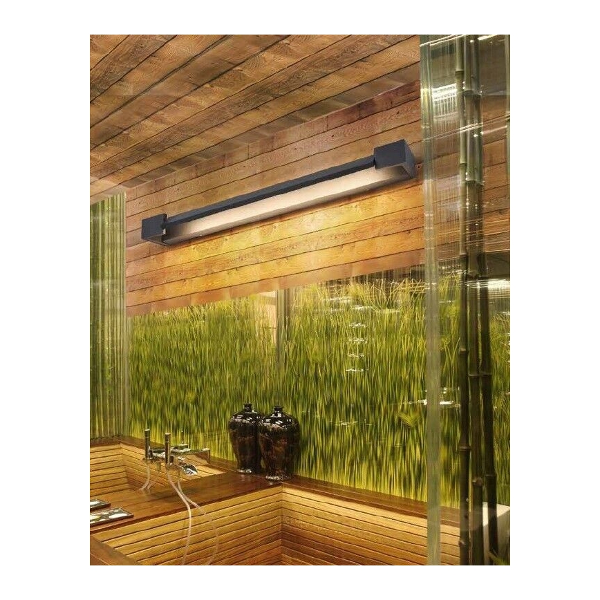 Dlhá obdĺžniková lampa svieti na drevenej stene v kúpeľni. Lampa je pripevnená k stene. Kúpeľňa má drevené prvky a zelenú stenu z vysokých tráv.