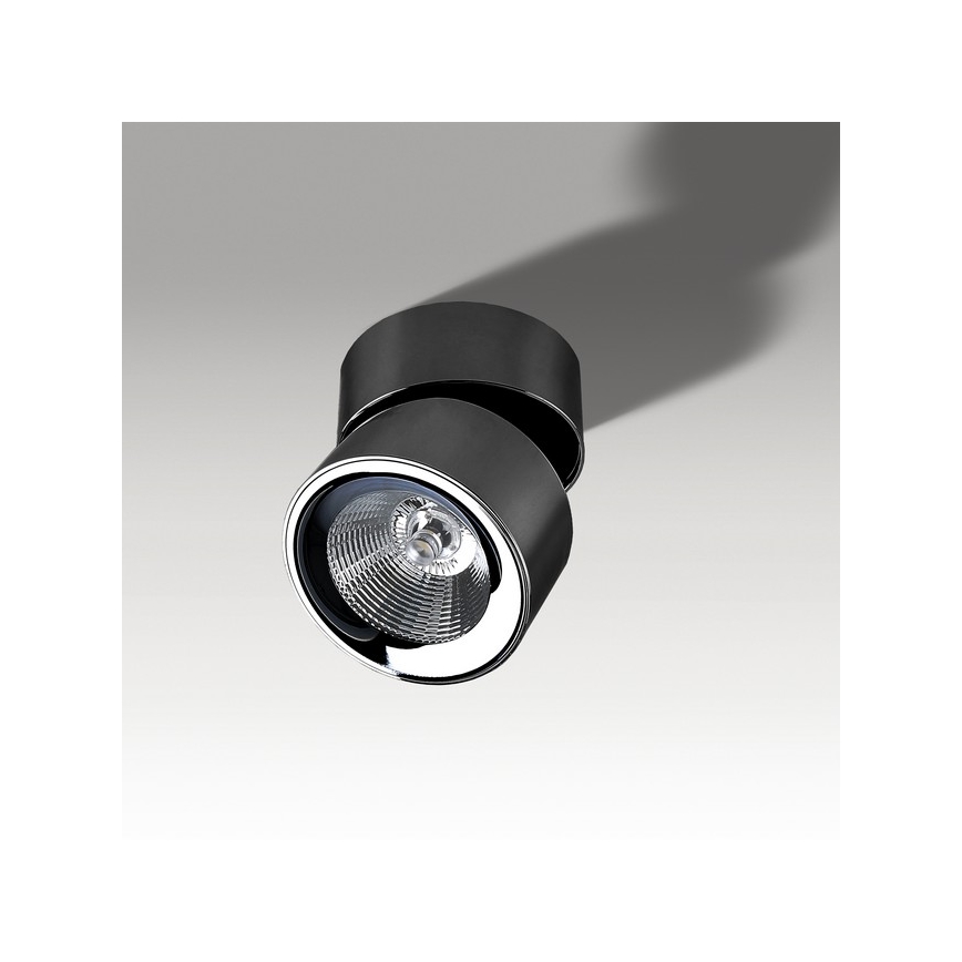 Svietidlo svieti na svetlo. Je otočné a má čierny kovový kryt. Nachádza sa na svetlom pozadí.