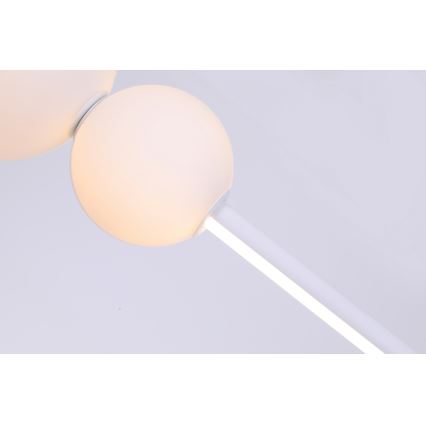 Biela lampa s guľovými tienidlami svieti. Dve gule sú pripojené k tenkej bielej tyči. Svetlo prechádza cez tyč.