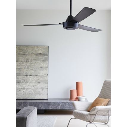 Čierny stropný ventilátor s tromi lopatkami rotuje v interiéri. Nachádza sa v obývacej izbe s nábytkom a dekoráciami.