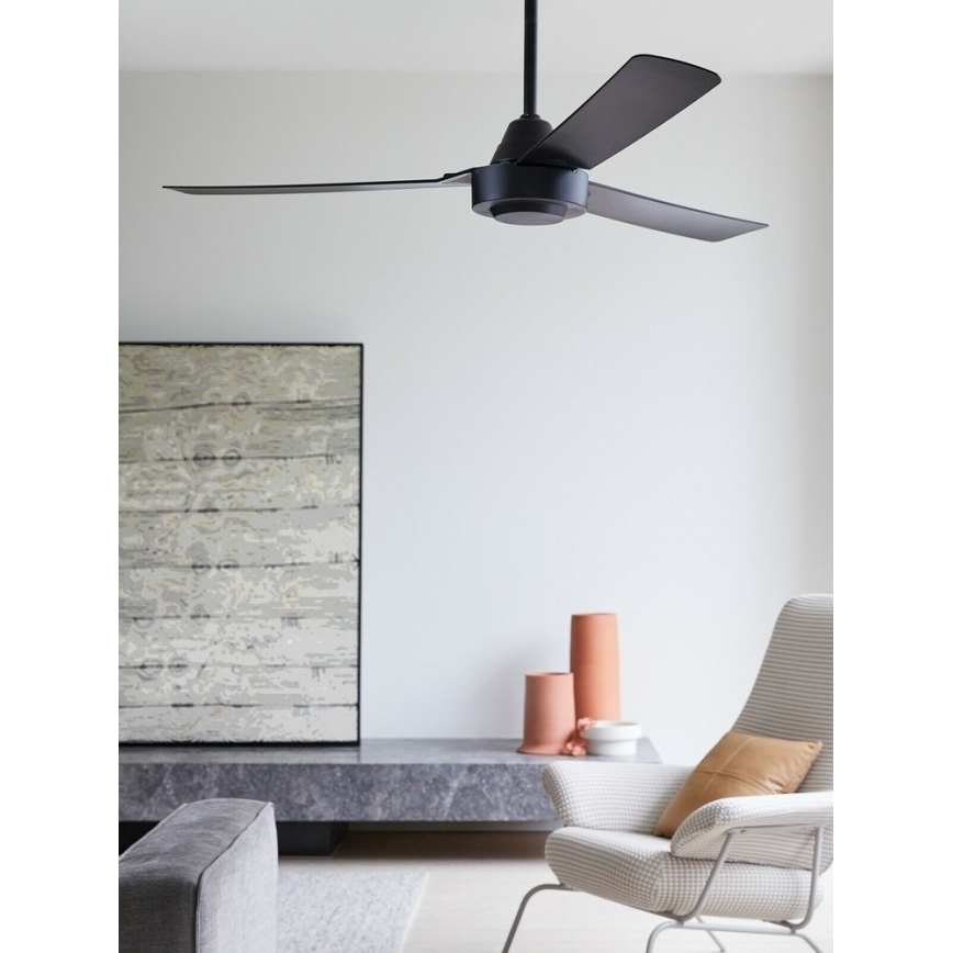 Čierny stropný ventilátor s tromi lopatkami rotuje v interiéri. Nachádza sa v obývacej izbe s nábytkom a dekoráciami.