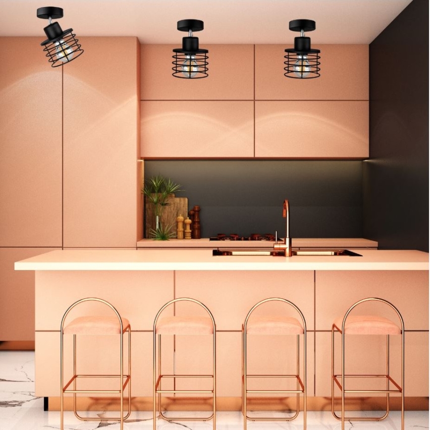 Tri stropné svietidlá s kovovými tienidlami visia v kuchyni. Svietidlá sú umiestnené nad kuchynským ostrovčekom s ružovými stoličkami.
