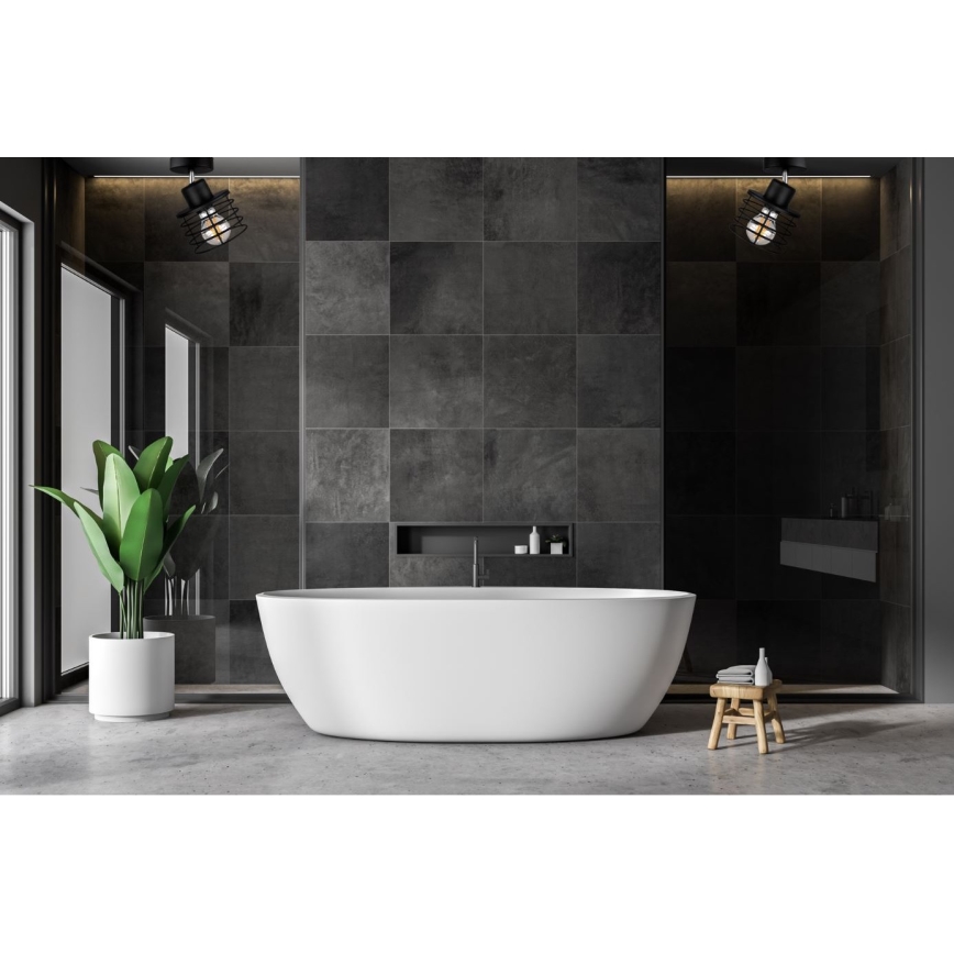 V kúpeľni s tmavými dlaždicami stojí voľne stojaca biela vaňa. Nad vaňou sú dve čierne svietidlá s kovovými tienidlami. V blízkosti vane je drevený stolík.