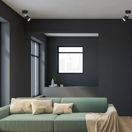 Svetlozelená pohovka stojí v tmavosivej miestnosti. Na pohovke sú béžové vankúše a prehodená je béžová deka. V pozadí sú tmavosivé steny a okná.