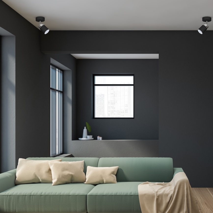 Svetlozelená pohovka stojí v tmavosivej miestnosti. Na pohovke sú béžové vankúše a prehodená je béžová deka. V pozadí sú tmavosivé steny a okná.