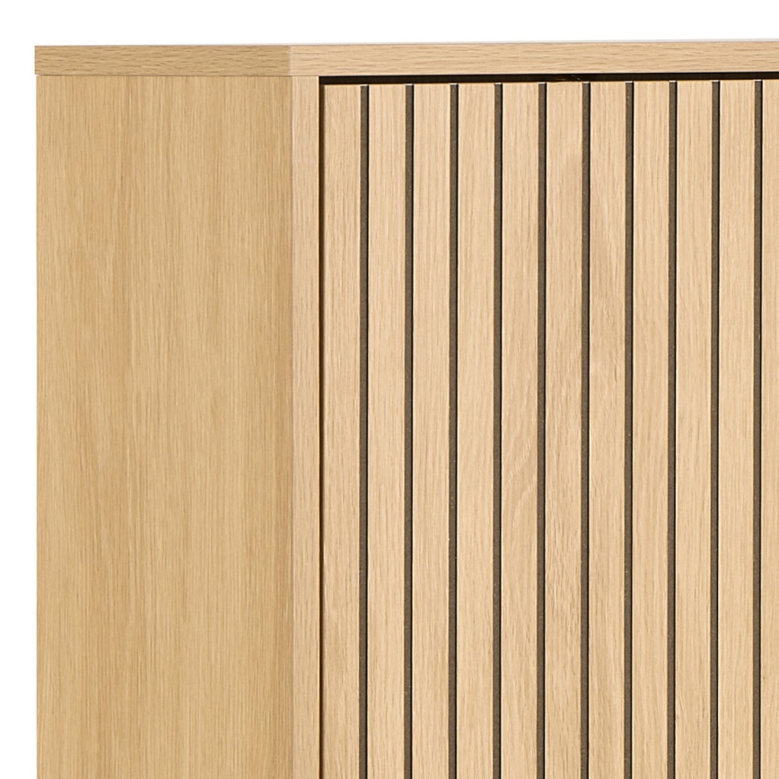 Drevená skrinka s vertikálnymi drážkami na dvierkach je zobrazená v detailnom zábere. Horná časť skrinky je rovná. Viditeľná je len časť skrinky.