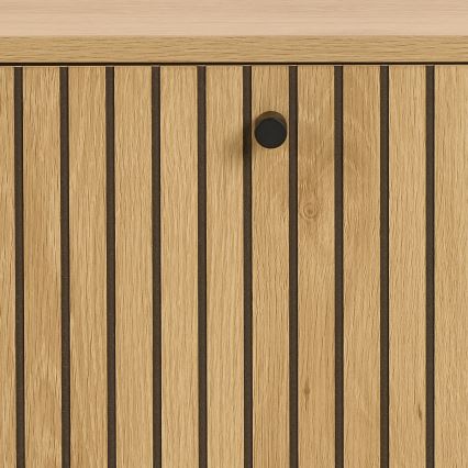 Drevené dvierka s vertikálnymi drážkami a čiernou kľučkou sú umiestnené na svetlom drevenom nábytku.