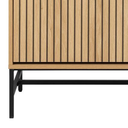 Drevená skrinka s vertikálnymi drážkami stojí na nízkych čiernych kovovaných nohách. Svetlo hnedá drevená dvierka sú zdobené tmavšími, tenkými vertikálnymi líniami.