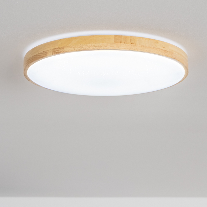 Svietidlo svieti na strope. Je okrúhle, s bielym difúzorom a dreveným rámom. Nachádza sa v svetlej miestnosti.