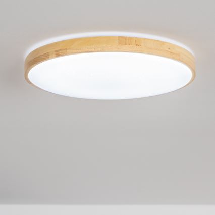 Svietidlo svieti na strope. Je okrúhle, s bielym difúzorom a dreveným rámom. Nachádza sa v svetlej miestnosti.