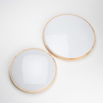 Dve kruhové svietidlá s dreveným rámom a bielym difúzorom sú položené na bielom podklade. Menšie svietidlo je umiestnené pod väčším.