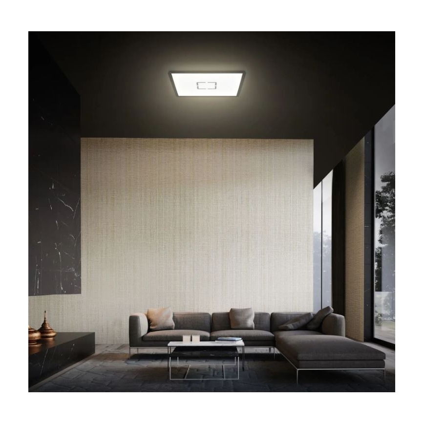 Stropné svetlo svieti v modernej obývacej izbe. Svetlo je štvorcové a zapnuté. Izba obsahuje rohovú sedačku a nízky konferenčný stolík.