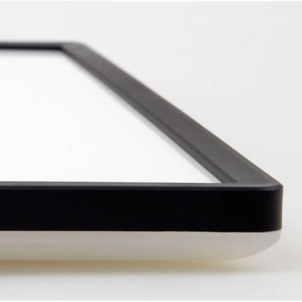 Obdĺžniková doska s bielym povrchom a čiernym rámom leží na svetlom podklade. Rám je hrubý a zreteľne viditeľný.