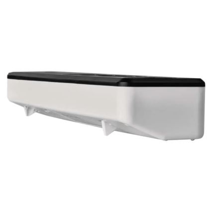 Dávkovač potravínarskej fólie je umiestnený na stene. Má biely plastový korpus s čiernym vrchnákom a štyrmi malými nožičkami na spodnej strane.