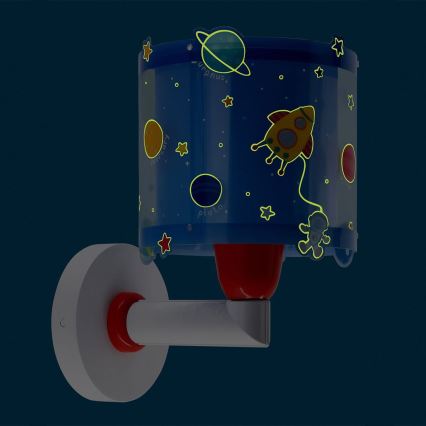 Nástenná lampa svieti. Na tienidle sú namaľované planéty (Pluto, Urán, Merkúr), raketa a hviezdy, ktoré žiarivo svietia v tme. Lampa je pripevnená na stenu.
