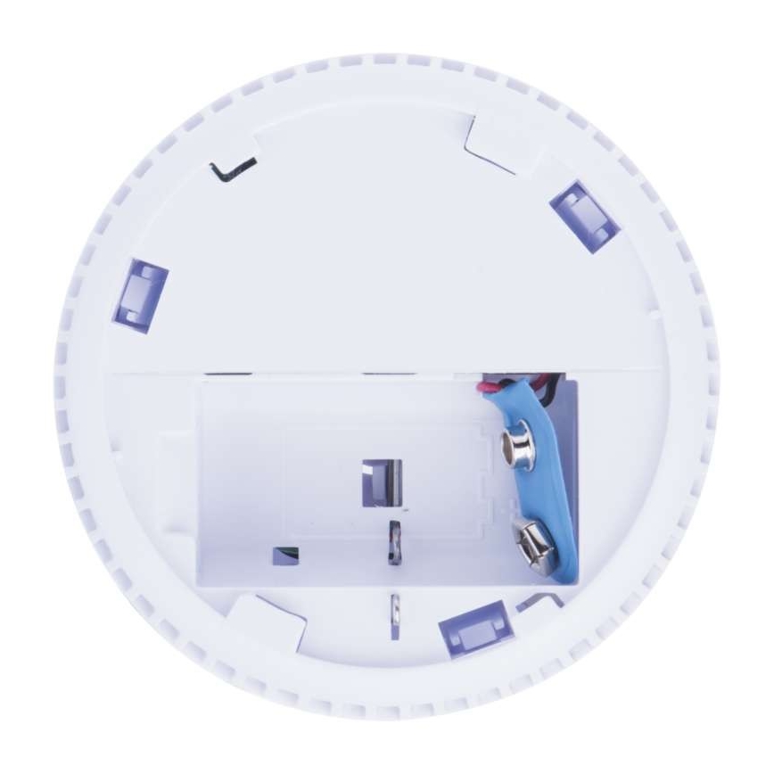 Biely kruhový detektor má otvorený kryt odhaľujúci batériový priestor s dvoma batériami. Viditeľné sú kontakty a drôty. Detektor je na bielom pozadí.