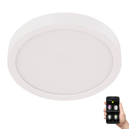Okrúhle stropné LED svetlo svieti. Ovládanie cez mobilnú aplikáciu zobrazenú na telefóne v ruke.