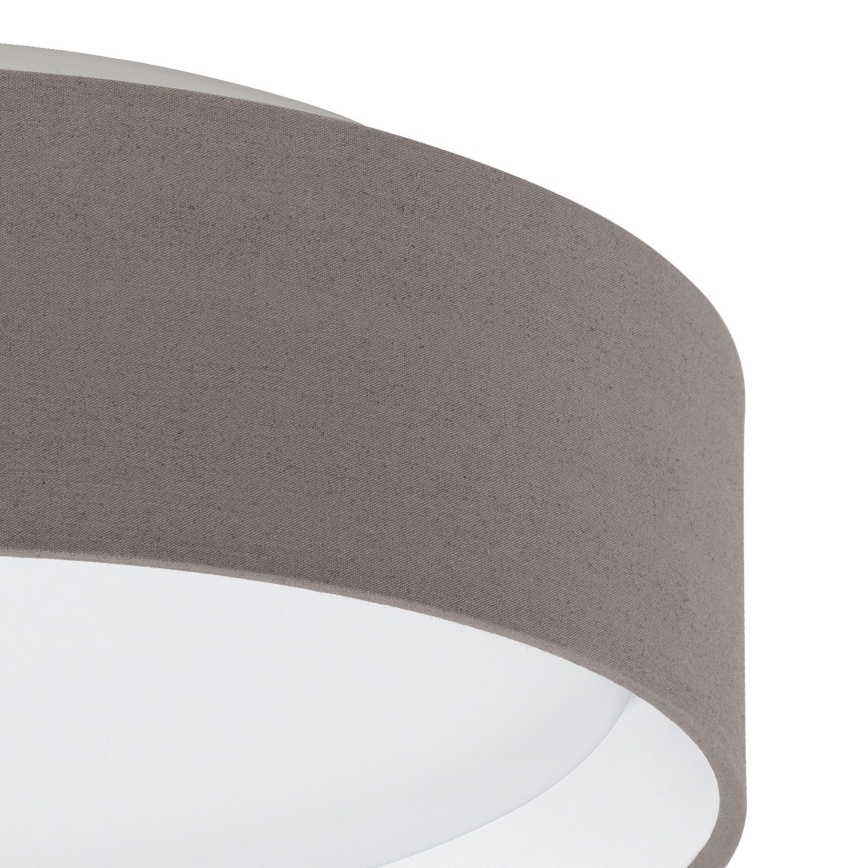 Svietidlo s textilným tienidlom svetlohnedej farby je zobrazené zblízka. Tienidlo je valcovitého tvaru, s vnútornou bielou časťou. Svietidlo je osvetľovacím telesom.