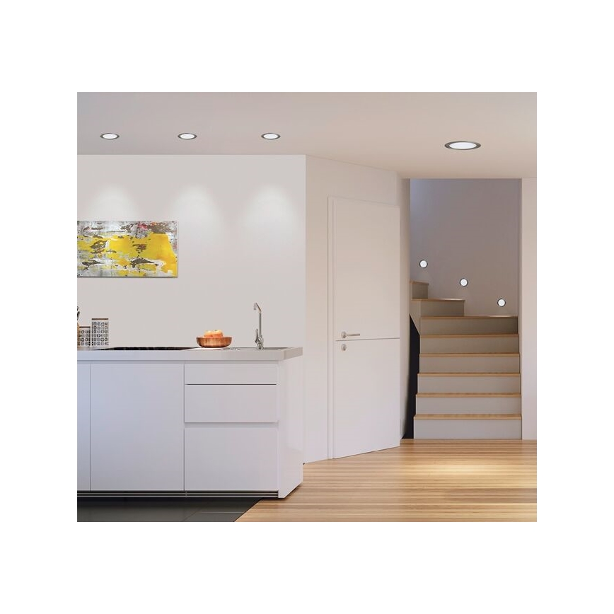 Moderná kuchynská linka s integrovaným drezom je osvetlená vstavanými bodovými svetlami. Vedľa sa nachádza schodisko s podobným osvetlením. V pozadí je obraz a svetlé drevené podlahy.