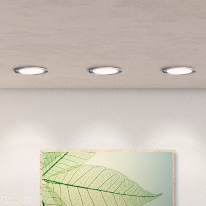 Tri vstavané kruhové svetlá svietia na svetlej stene. Pod nimi visí obraz listov. BEAU MOTICA.