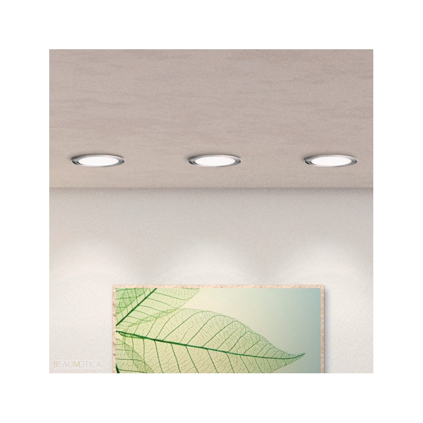 Tri vstavané kruhové svetlá svietia na svetlej stene. Pod nimi visí obraz listov. BEAU MOTICA.