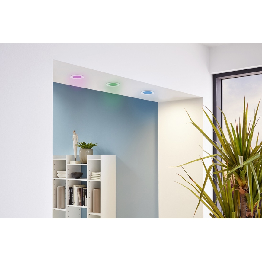 Tri kruhové farebné LED svetlá svietia na strope miestnosti. Svetlá vyžarujú fialovú, tyrkysovú a modrú farbu. Miestnosť obsahuje bielu knižnicu a veľkú izbovú rastlinu.