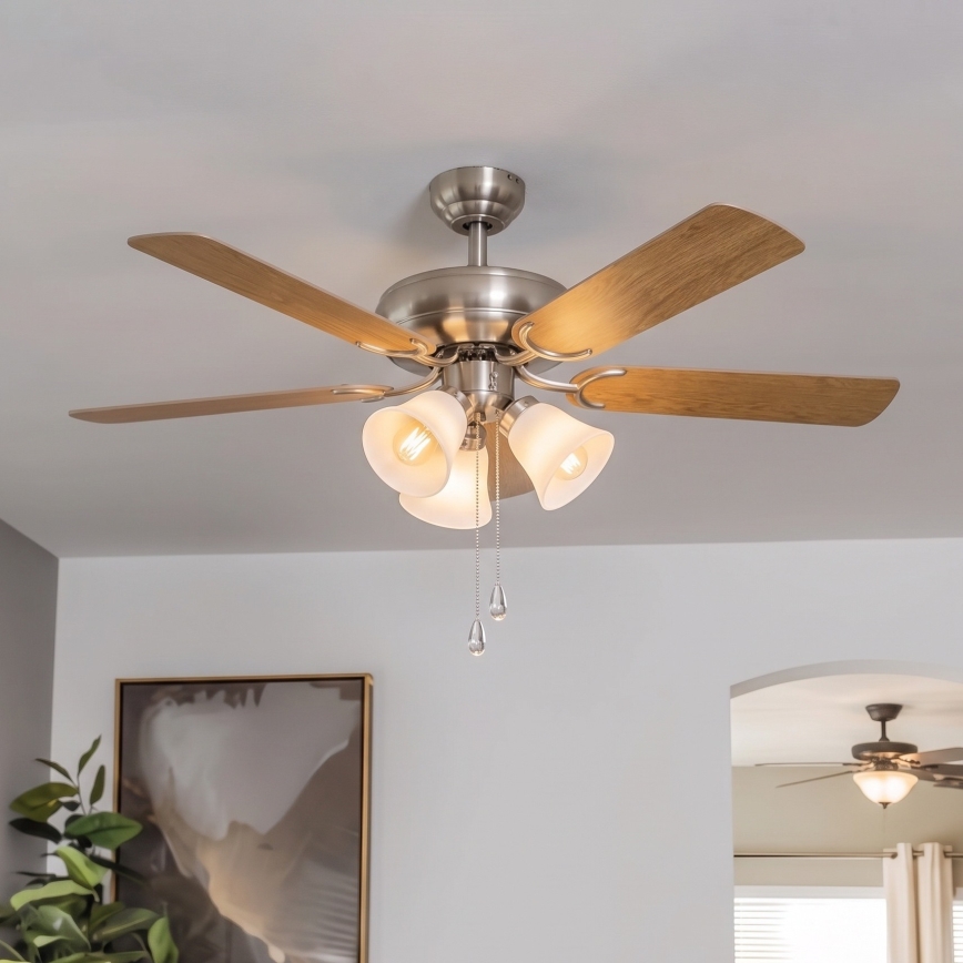 Stropný ventilátor s piatimi lopatkami a tromi svetlami rotuje na bielom pozadí. Lopaty sú svetlosivé, telo ventilátora je svetlokovové. Svetlá sú mliečne, s drobnými ozdobnými príveskami.
