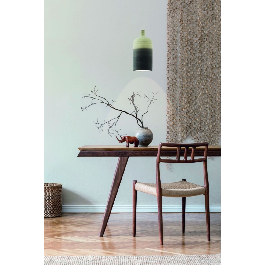 Keramická lampa svieti nad dreveným stolom. Na stole je váza s konármi a soška nosorožca. Stolička s pleteným sedákom je umiestnená pri stole.