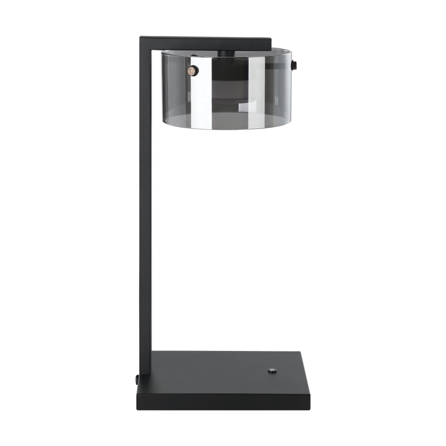Stolová lampa s čiernym kovový rámom a priehľadným, tmavosivým skleneným tienidlom stojí na čiernej štvorcovej základni.