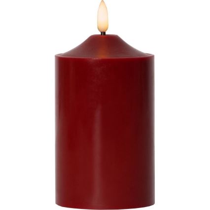 Elektrická sviečka s červeným voskom horí. Má realisticky vyzerajúci plameň. Sviečka je umiestnená na bielom pozadí.
