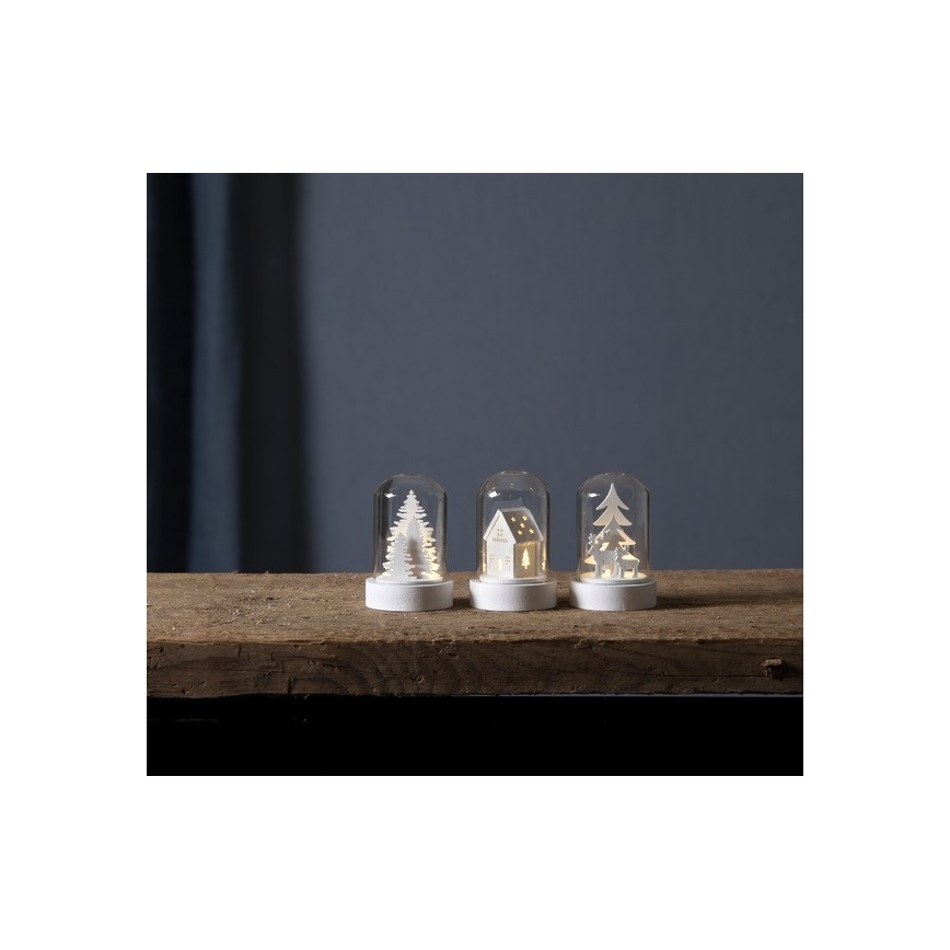 Tri malé sklené dómy s bielymi drevenými motívmi (stromčeky, domček, soby) a vnútorným LED osvetlením stoja na drevenom povrchu.