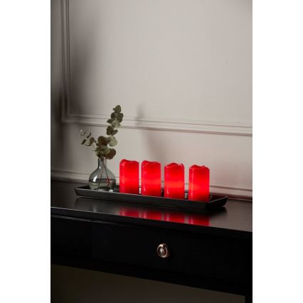 Červené LED sviečky stoja na čiernej podložke. Sviečky svietia. Vedľa nich je váza s eukalyptom. Všetko je na tmavom nábytku.