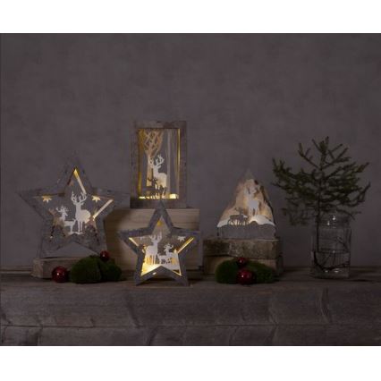 Drevené hviezdne a obdĺžnikové svietniky s vyrezávanými jelenmi svietia. Stoja na drevenom podklade s ihličnatým stromčekom a ozdobami.